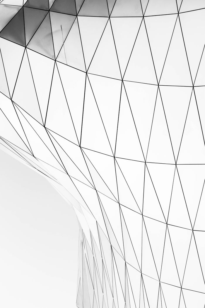 services-01 Close-up of a modern glass facade with geometric triangular patterns, showcasing contemporary architectural design.