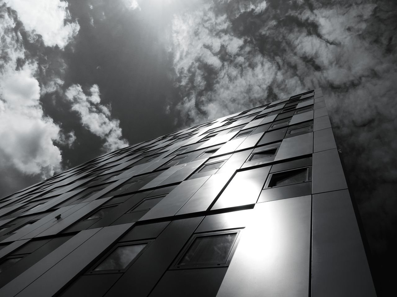 services-06 Low angle view of a modern building with reflective windows under a dramatic cloudy sky.